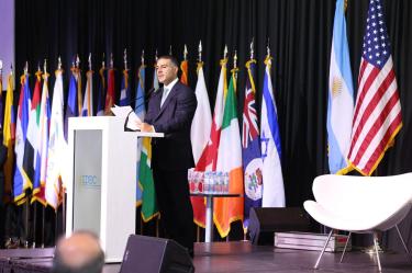 Omar García Harfuch habla en un podio durante la conferencia IDEC en Buenos Aires, con banderas de distintos países al fondo.