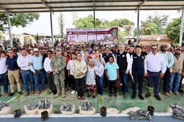 Autoridades, productores y habitantes participan en una entrega de apoyos agrícolas con plantas e insumos colocados frente al grupo.