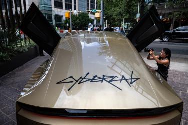 Tesla Cybercab exhibido en Austin, Texas, con sus puertas abiertas mientras una fotógrafa registra el vehículo autónomo.