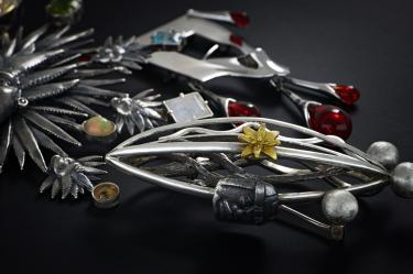 Broches de joyería mexicana en plata, con formas orgánicas, piedras de colores y detalles florales sobre un fondo negro.
