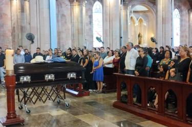 Familiares y asistentes permanecen de pie junto a un féretro durante una ceremonia funeraria dentro de una iglesia.