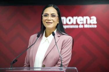 Ariadna Montiel, dirigente de Morena, habla ante dos micrófonos en un podio con el logotipo del partido al fondo.