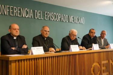 Obispos de la Conferencia del Episcopado Mexicano participan en una reunión ante una mesa con micrófonos y documentos.