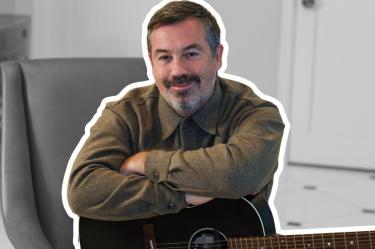 Duncan Sheik sentado junto a una guitarra acústica en un espacio interior.