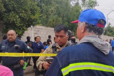 Fotografía de la investigación policial acordonada con cinta amarilla de seguridad frente a la Secundaria 13 de Torreón, Coahuila, tras un ataque armado perpetrado por exalumnos. Varios agentes de policía y civiles están presentes. Un oficial con equipo táctico mira su teléfono móvil detrás de la cinta de seguridad.