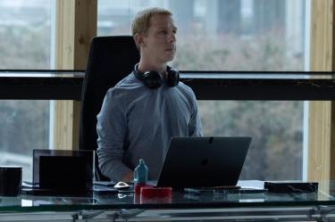 Jeremy Strong como Mark Zuckerberg sentado frente a una laptop en una oficina en El poder de la red.