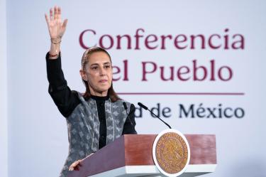 La presidenta Claudia Sheinbaum levantando la mano desde el atril durante la Conferencia del Pueblo sobre temas energéticos.
