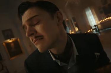 Hombre con traje aparece en una habitación iluminada por velas durante una escena de American Horror Story 13.