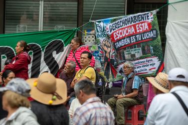 arias personas sentadas y reunidas en un plantón debajo de una lona que dice "Derechohabiente escucha esta también es tu lucha!!" junto al logotipo del IMSS.