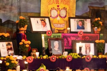 Ofrenda de Día de Muertos de varios niveles con fotografías, calavera amarilla, veladoras, flores de cempasúchil y frutas.