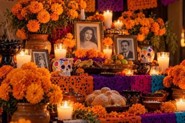 Ofrenda de Día de Muertos con retratos familiares, flores de cempasúchil, veladoras, calaveritas, fruta y pan de muerto.