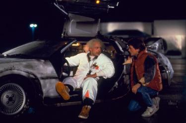 Doc Brown sentado en el DeLorean conversa con Marty McFly durante una escena nocturna de Volver al futuro.