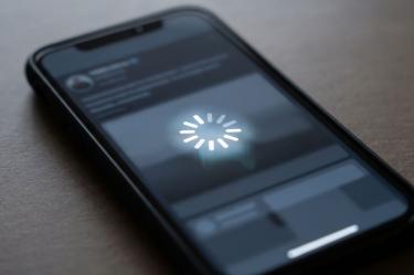Celular negro sobre una mesa con un símbolo de carga en la pantalla que representa un teléfono trabado.