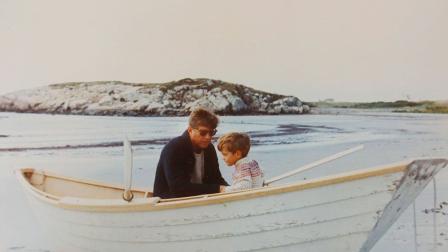 Sentados en un bote están el ex presidente John F. Kennedy y su hijo John Jr. en la playa Bailey, en Rhode Island.